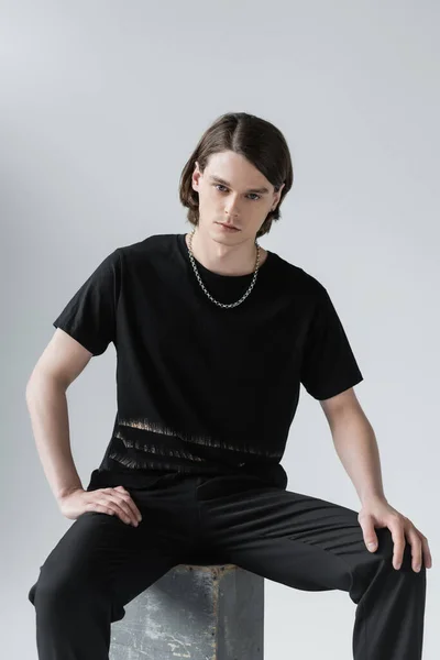 Young brunette man sitting on concrete block isolated on grey — Stock Photo