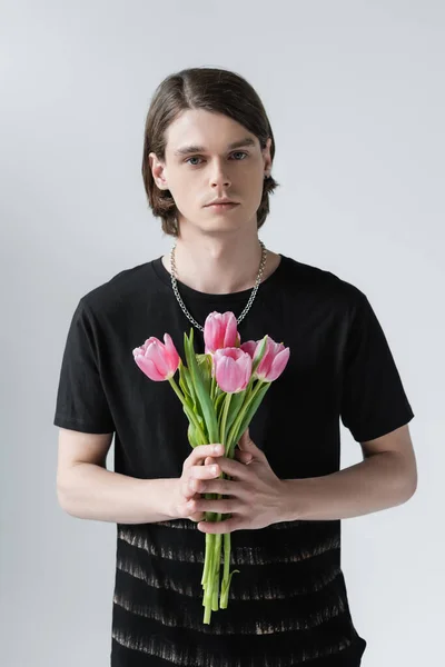 Молодой брюнетка мужчина держит тюльпаны изолированы на серый — стоковое фото