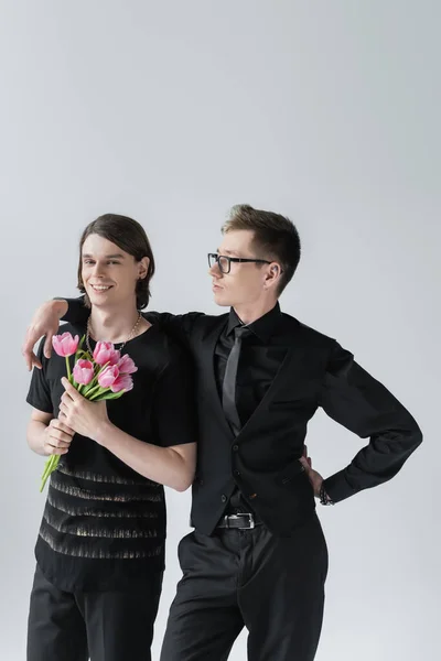 Gay in formal wear hugging boyfriend with tulips isolated on grey — Stock Photo