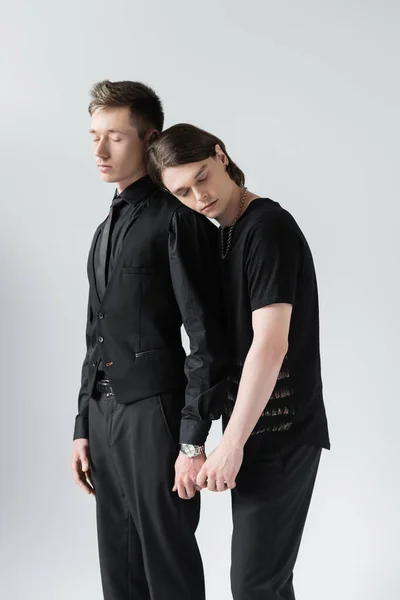 Joven pareja gay con los ojos cerrados sosteniendo las manos aisladas en gris - foto de stock