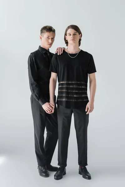 Full length of stylish gay couple holding hands on grey background — Stock Photo