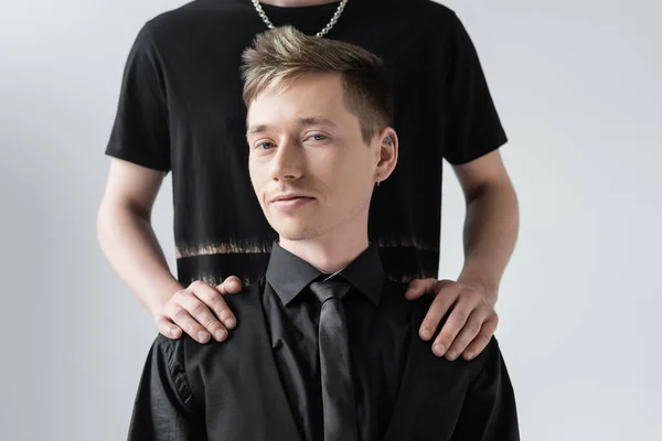 Молодий чоловік обіймає хлопця в офіційному одязі ізольовано на сірому — стокове фото