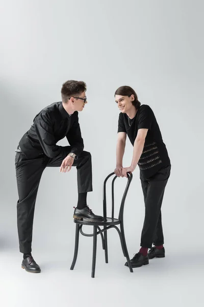 Smiling gay couple talking near chair on grey background — Stock Photo