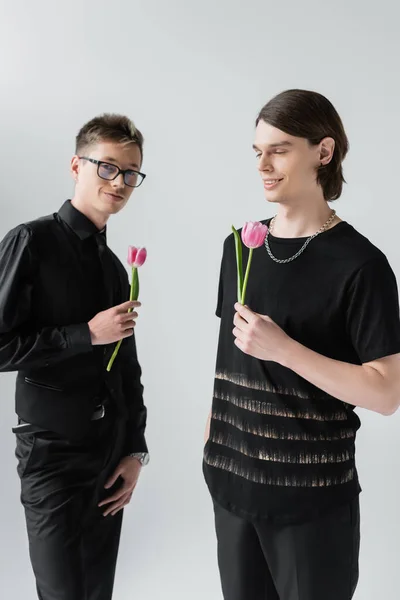 Positive gay couple holding tulips isolated on grey — Stock Photo