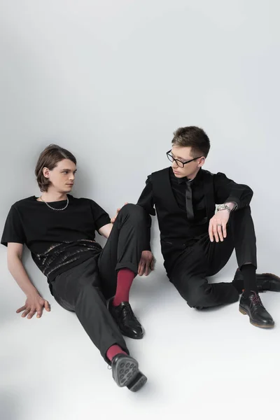 Homosexual couple looking at each other while sitting on grey background — Stock Photo