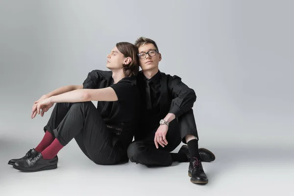 Joven y elegante pareja homosexual sentada sobre fondo gris - foto de stock