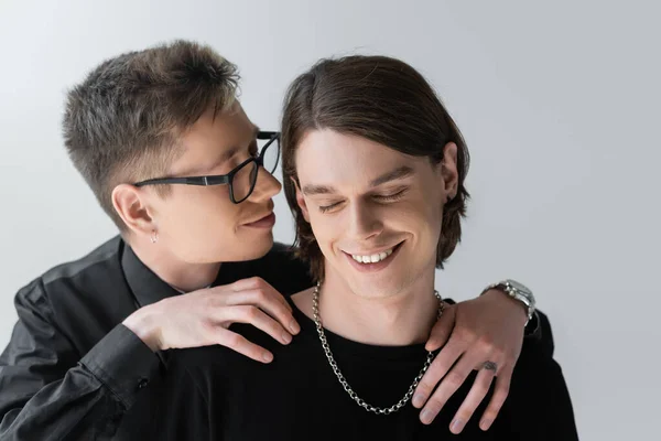 Homme aux lunettes étreignant petit ami souriant aux yeux fermés isolé sur gris — Photo de stock