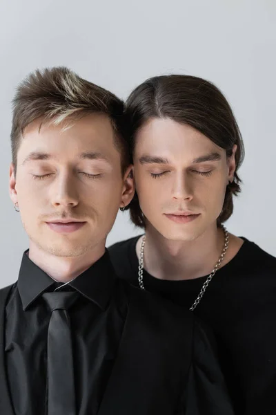 Porträt eines jungen homosexuellen Paares, das mit geschlossenen Augen auf grau isoliert steht — Stockfoto