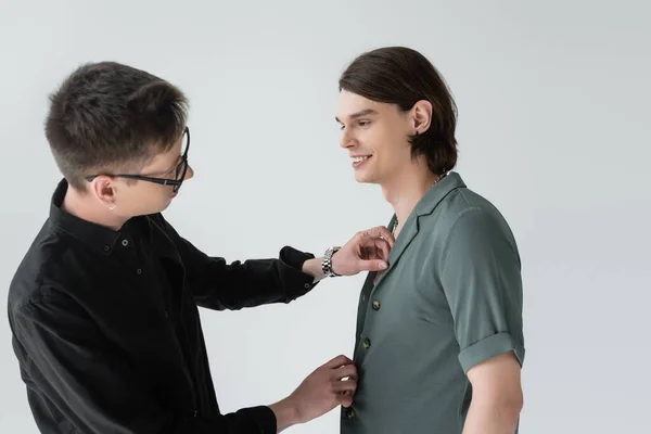 Side view of young gay in eyeglasses adjusting shirt on boyfriend isolated on grey — Stock Photo