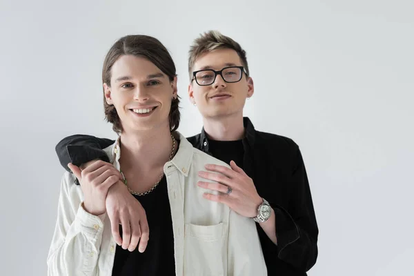 Homosexual man embracing smiling and stylish boyfriend isolated on grey — Stock Photo