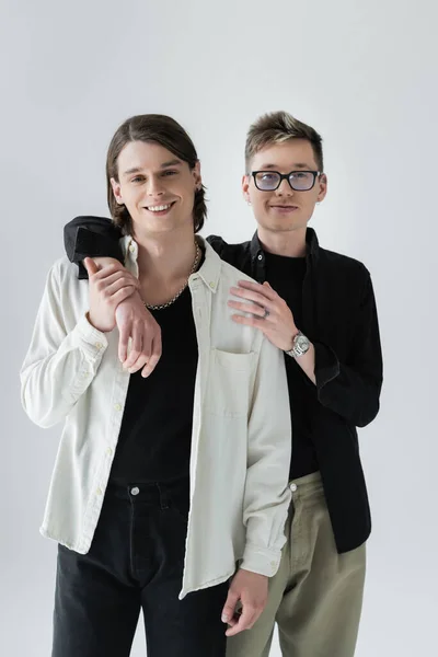 Trendy gleichgeschlechtliches Paar umarmt und blickt isoliert in die Kamera auf grau — Stockfoto