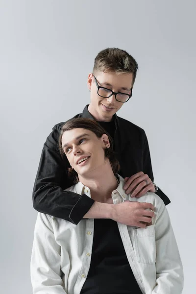 Young gay in eyeglasses embracing stylish boyfriend isolated on grey — Stock Photo