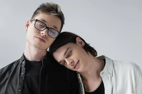 Retrato de pareja gay joven cerrando los ojos mientras está de pie aislado en gris - foto de stock