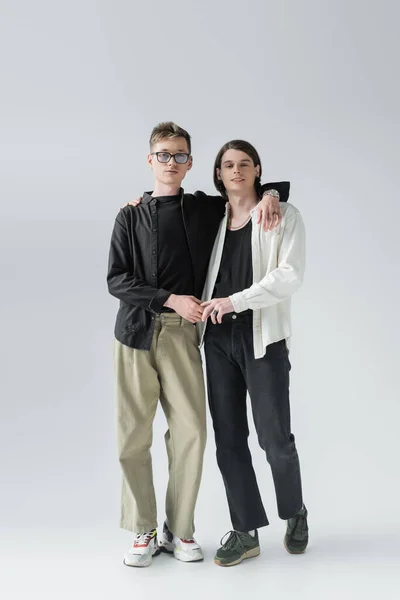 Longitud completa de gay pareja cogido de la mano y abrazando en gris fondo - foto de stock