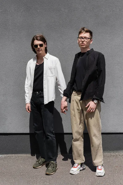 Trendy homosexual couple holding hands near building outdoors — Stock Photo