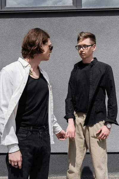 Young same sex couple holding hands and looking at each other near building outdoors — Stock Photo