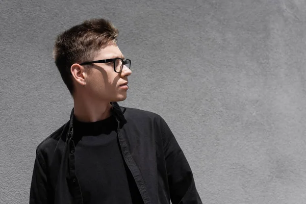 Young man in eyeglasses and black clothes looking away on urban street — Stock Photo