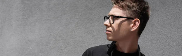 Young man in eyeglasses looking away near building outdoors, banner — Stock Photo