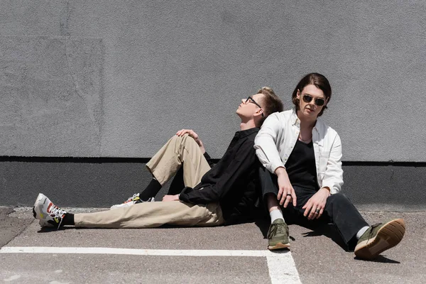 Joven pareja del mismo sexo sentado cerca del edificio en la calle urbana - foto de stock