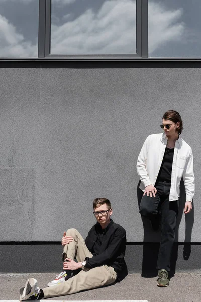 Young stylish same sex couple posing near building on urban street — Stock Photo