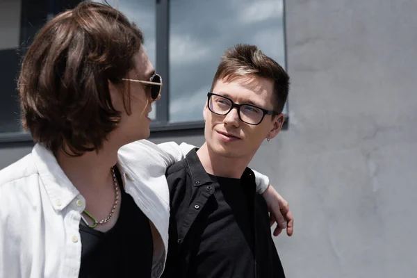 Hombre con estilo en gafas de sol abrazando novio en la calle urbana - foto de stock