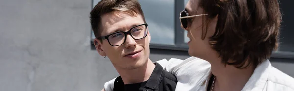 Young man in sunglasses hugging young boyfriend on urban street, banner — Stock Photo