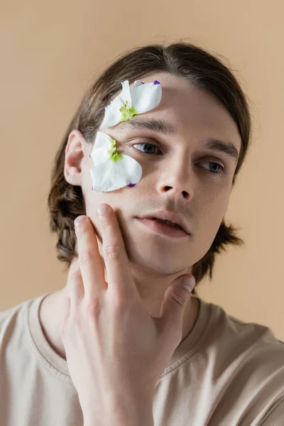 Joven con flor en la cara mirando hacia otro lado aislado en beige - foto de stock