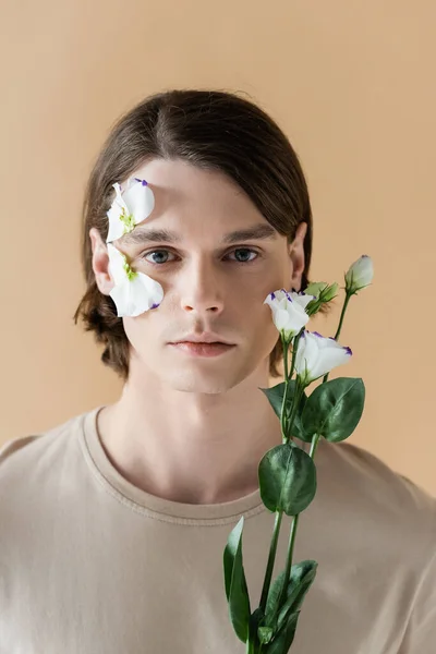 Brunette homme avec fleur sur le visage tenant eustome isolé sur beige — Photo de stock