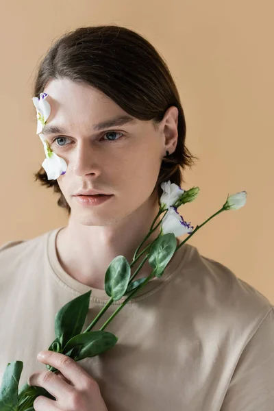 Retrato de un joven sosteniendo una flor de eustoma aislada en beige - foto de stock