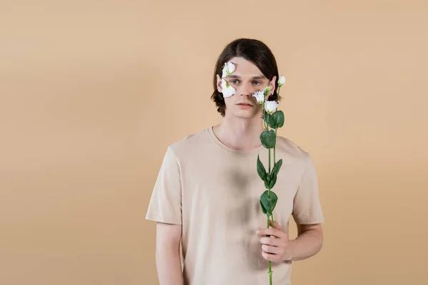 Молодой брюнетка мужчина держит цветок эустомы изолированы на бежевый — стоковое фото