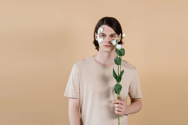 Jovem morena homem segurando flor eustoma isolado no bege — Fotografia de Stock