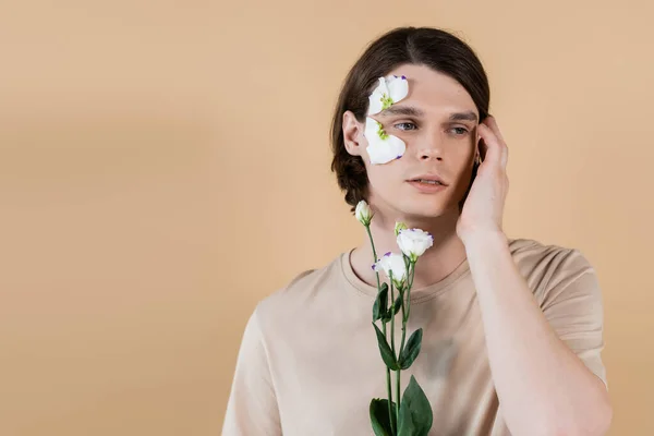 Portrait of young man holding eustoma and touching face isolated on beige — Stock Photo