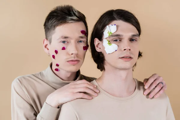 Portrait of gay couple with petals on face looking at camera isolated on beige — Stock Photo