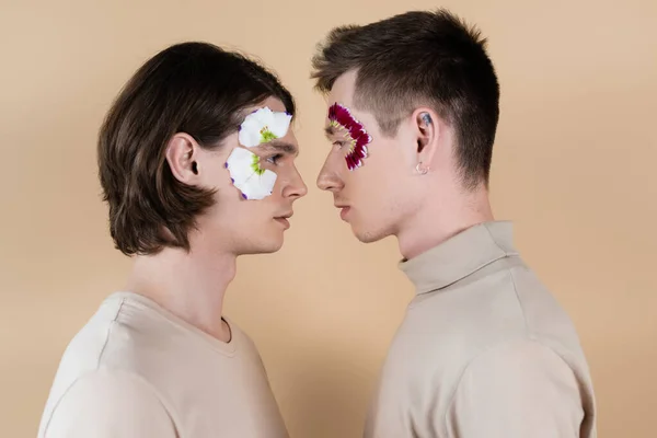 Vue latérale du couple gay avec des pétales floraux sur les visages sur beige — Photo de stock
