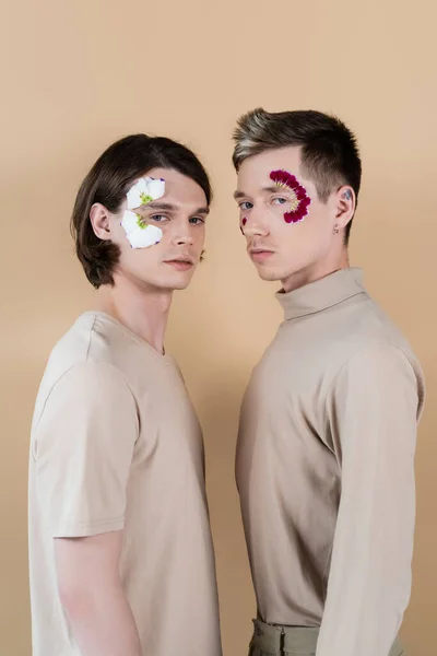 Young homosexual couple with petals on faces looking at camera isolated on beige — Stock Photo