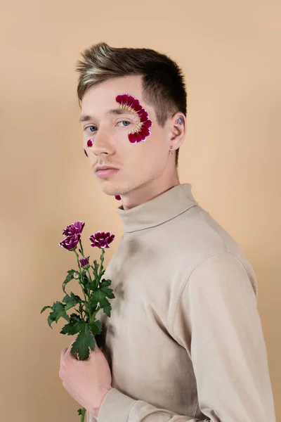 Portrait of young man with petals on face holding flowers isolated on beige — Stock Photo