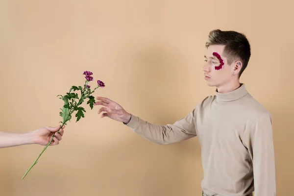 Mann hält Chrysanthemen neben Freund mit Blütenblättern im Gesicht auf beige — Stockfoto