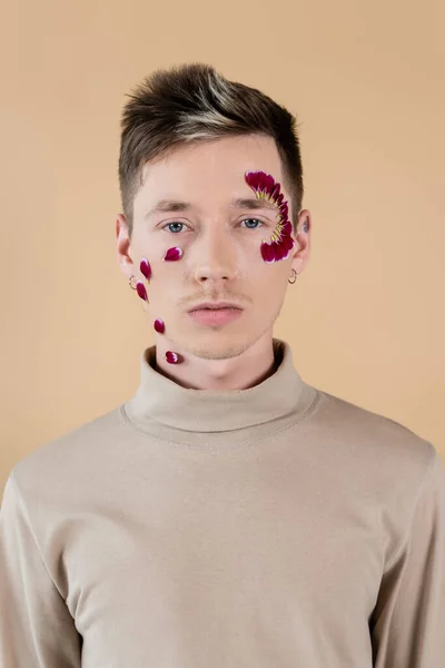 Ritratto di giovane uomo con petali sul viso guardando la macchina fotografica isolata sul beige — Foto stock