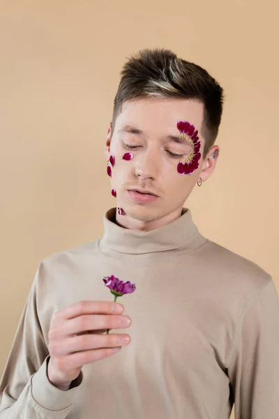 Чоловік з пелюстками на обличчі тримає квітку хризантеми ізольовані на бежевому — стокове фото