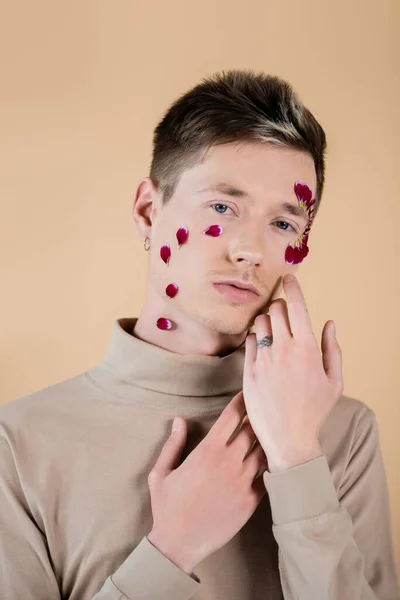 Joven con pétalos en la cara posando aislado en beige - foto de stock