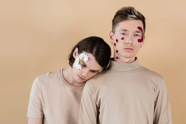 Schwules Paar mit Blütenblättern im Gesicht steht isoliert auf beige — Stockfoto