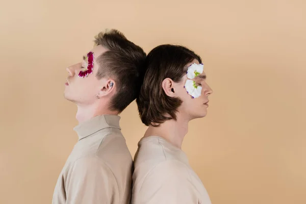 Side view of gay couple with petals on faces standing back to back isolated on beige — Stock Photo