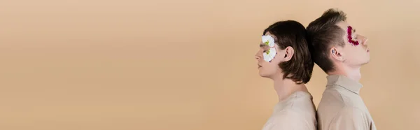 Same sex couple with petals on faces standing back to back isolated on beige, banner — Stock Photo