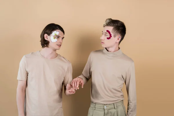 Gay couple with flower petals on faces holding hands on beige — Stock Photo