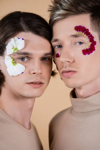 Ritratto di giovani partner omosessuali con petali floreali su volti isolati su beige — Foto stock