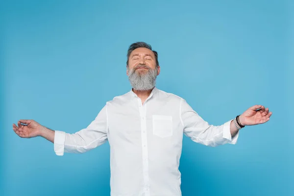 Gurú maestro barbudo con los ojos cerrados mostrando gyan mudra mientras medita aislado en azul - foto de stock