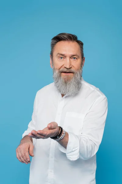 Bärtiger spiritueller Guru blickt in die Kamera und zeigt mit isolierter Hand auf blau — Stockfoto