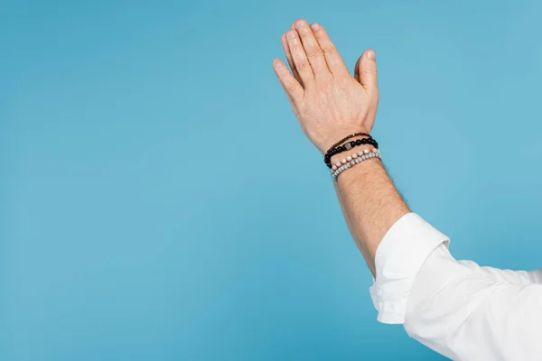 Vista recortada del hombre en pulseras de cuentas en las manos de oración aislado en azul - foto de stock