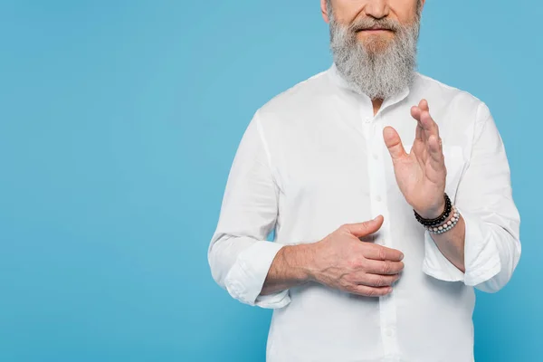 Vista cortada de guru treinador com barba cinza mostrando gesto de bênção isolado em azul — Fotografia de Stock