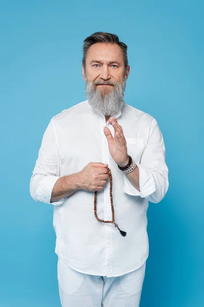 Grauhaariger Meister-Guru mit Rosenkranz zeigt Segensgeste isoliert auf blauem Grund — Stockfoto